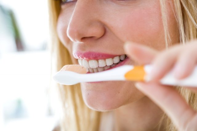 Portrait of pretty young blonde woman cleaning her teeth.
